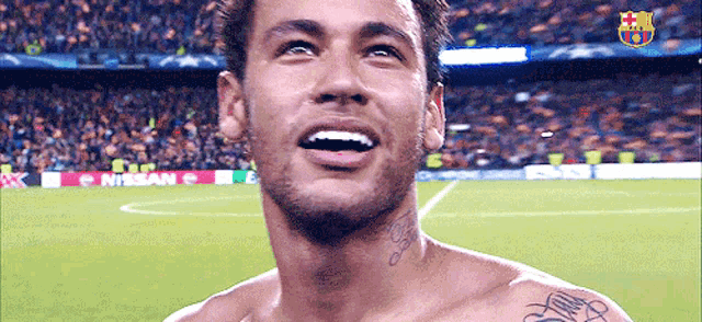 a shirtless man with a tattoo on his neck is smiling on a soccer field sponsored by nissan