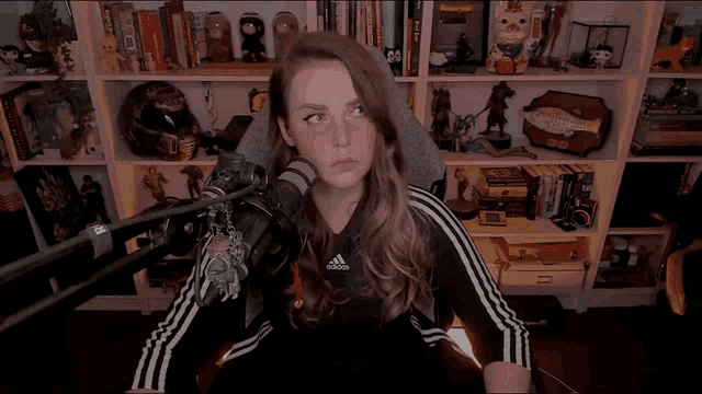 a woman wearing a black adidas shirt stands in front of a microphone