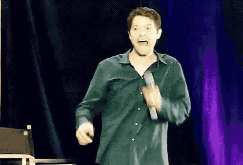 a man in a green shirt is standing on a stage with a microphone in his hand .