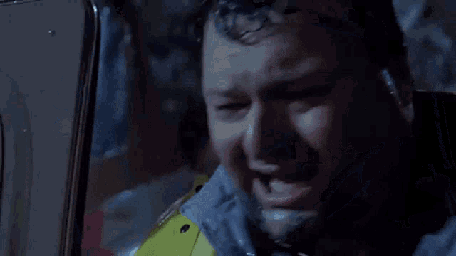 a man in a yellow raincoat is sitting in a car in the rain .