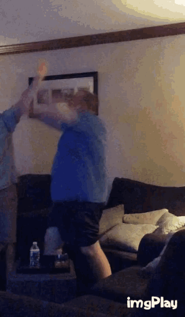 a man in a blue shirt is dancing in a living room with imgplay written on the bottom right