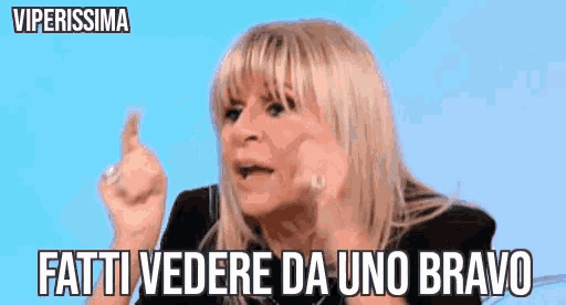 a woman with blonde hair and bangs is giving a thumbs up and says fatti vedere da uno bravo .