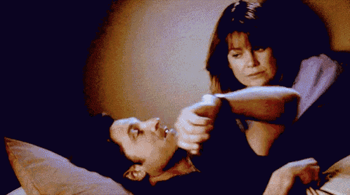 a man and a woman are laying in bed and the woman is holding the man 's hand