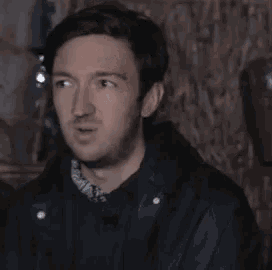 a man in a black jacket is sitting in a dark room .