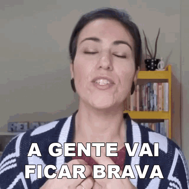 a woman says " a gente vai ficar brava " in front of a yellow bookshelf