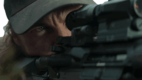 a man in a hat looking through a rifle scope