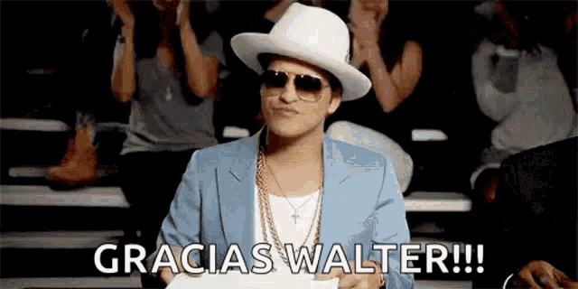 a man wearing a white hat and sunglasses is sitting in front of a crowd and says gracias walter !!!