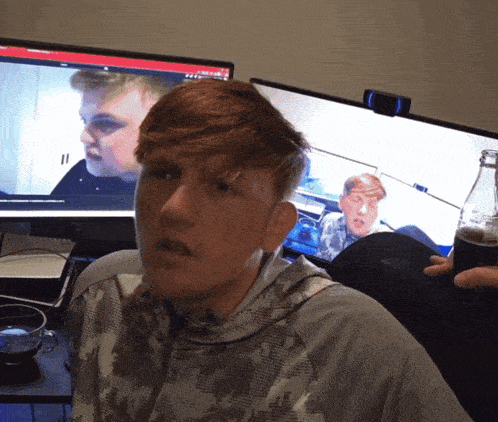 a man sitting in front of a computer screen with a bottle of coke in front of him