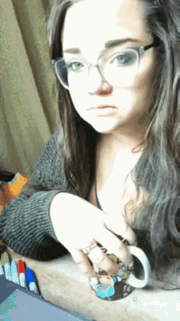 a woman wearing glasses and a ring holds a coffee mug