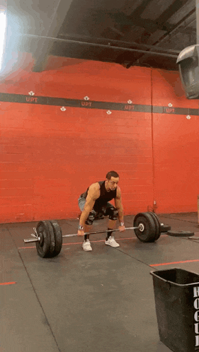 a man is lifting a barbell in a gym with the word upt on the wall behind him