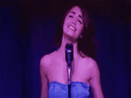 a woman in a blue dress is singing into a microphone with her arms outstretched