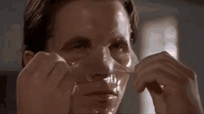 a close up of a man peeling off a mask from his face .