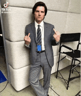a man in a suit and tie giving the middle finger in front of a chair