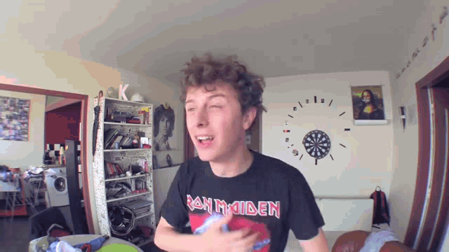 a man wearing an iron maiden shirt stands in front of a dartboard