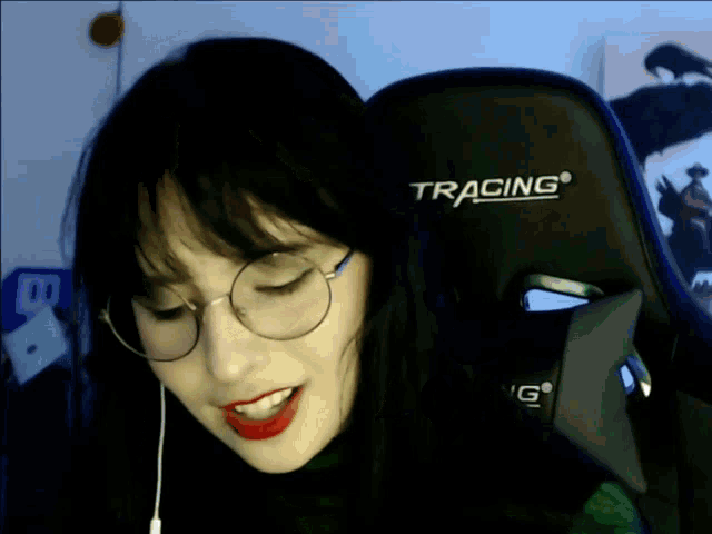 a woman wearing glasses is sitting in a tracing gaming chair