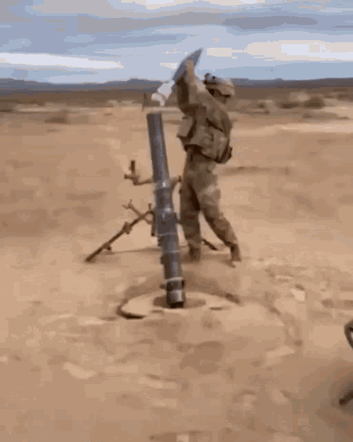 a soldier is kneeling down next to a mortar in the dirt