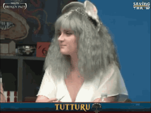 a woman in a white top is sitting in front of a screen that says tutturu