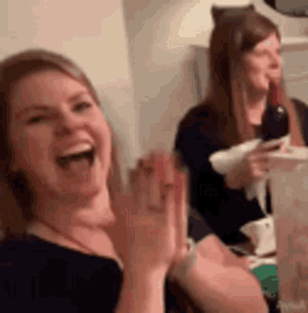 a woman is laughing while sitting at a table with a bottle of wine in her hand .