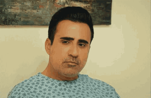a man in a hospital gown looks at the camera with a serious look on his face