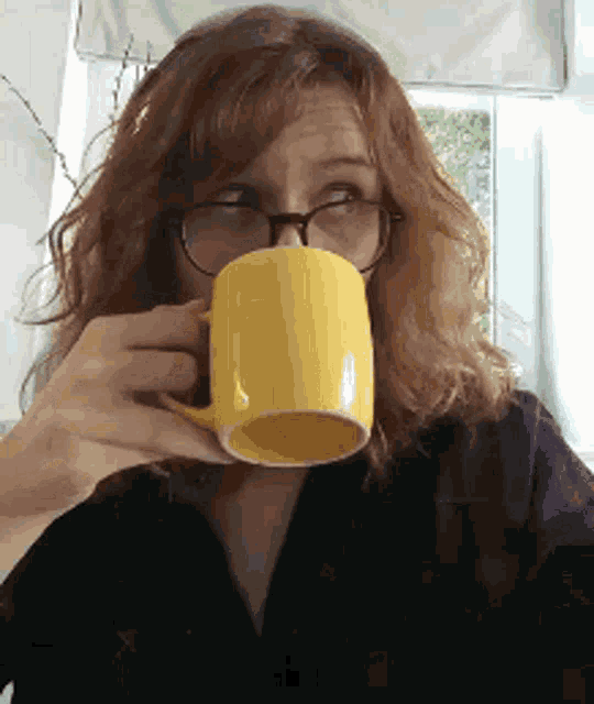 a woman wearing glasses is drinking from a yellow coffee mug