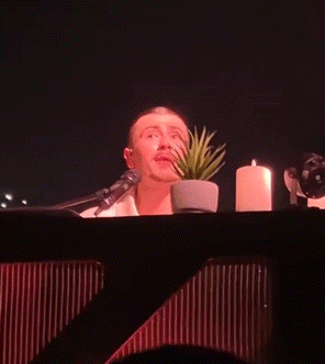 a man singing into a microphone with a potted plant and candles in the background