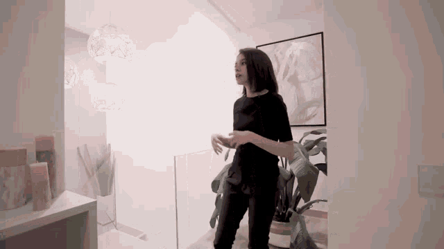 a woman in a black shirt is standing in a hallway with a plant .