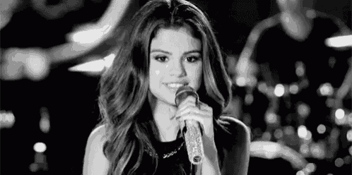 a woman is singing into a microphone on a stage in a black and white photo .