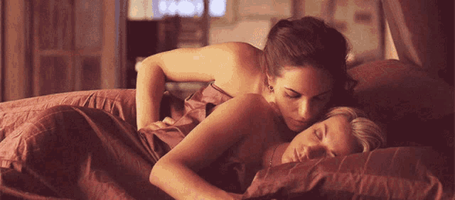two women are laying on a bed with their heads together