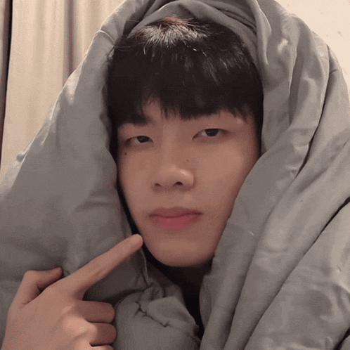 a young man is wrapped in a blanket and pointing to his face