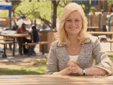 a woman is smiling while sitting at a picnic table in a park .