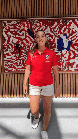 a woman in a red shirt and white shorts is standing in front of a large painting .