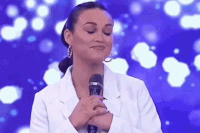 a woman in a white jacket is standing in front of a microphone with her hands on her chest .