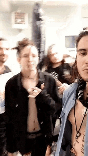a group of people are standing in a room and one of them has a tattoo on his chest that says ' i '