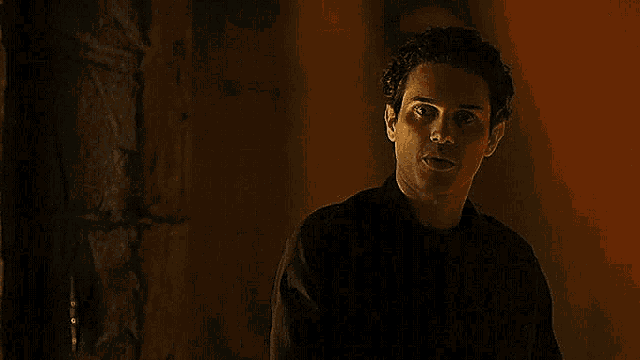 a man in a black shirt is standing in a dark room with a red light behind him .