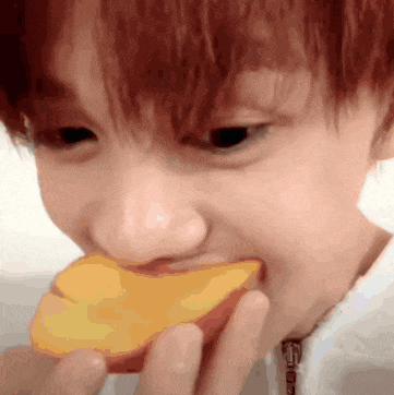 a young boy is eating a slice of peach .