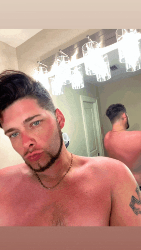 a shirtless man with a tattoo on his arm takes a selfie in front of a mirror