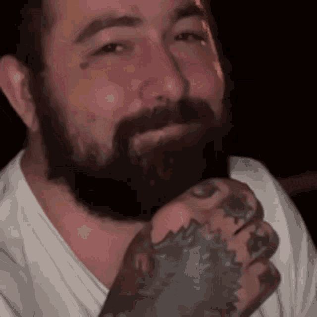a man with a beard and a tattoo on his hand is smiling and looking at the camera .