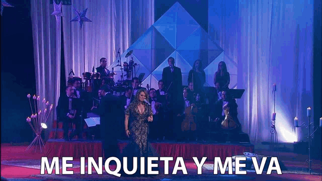 a woman singing on a stage with the words me inquieta y me va behind her