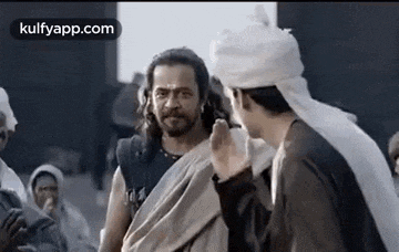 a man in a white turban is talking to another man in a crowd of people .