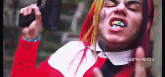 a man with a rainbow colored teeth is holding a gun in his hand while wearing a red hoodie .