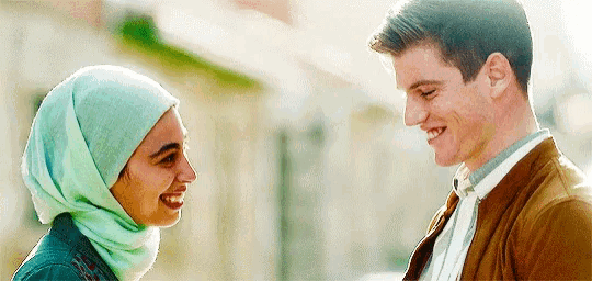 a man and a woman are smiling and looking at each other . the woman is wearing a hijab .