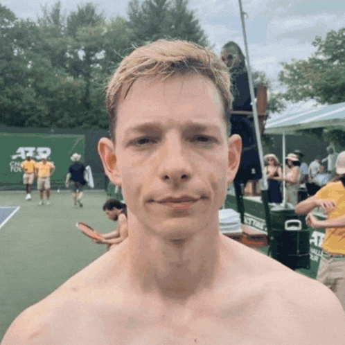 a shirtless man stands in front of a tennis court that has atp written on it
