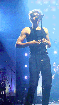 a man without a shirt is singing into a microphone on stage