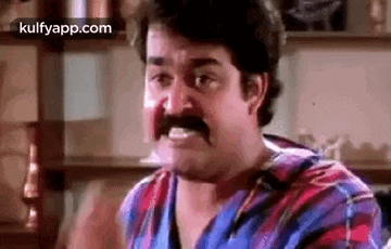 a man with a mustache is making a funny face while sitting in a room .