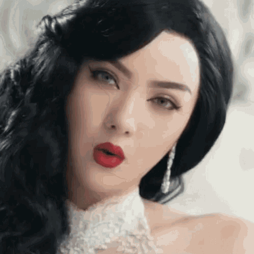 a woman with long black hair and red lipstick is wearing a white lace collar and earrings .