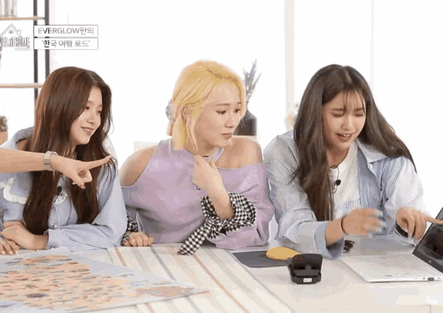 three girls are sitting at a table with a sign that says everglow on it