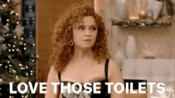 a woman with curly hair is standing in front of a christmas tree with the words `` love those toilets '' .