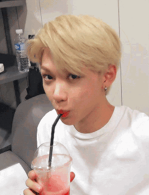 a young man drinking from a cup with a straw in his mouth