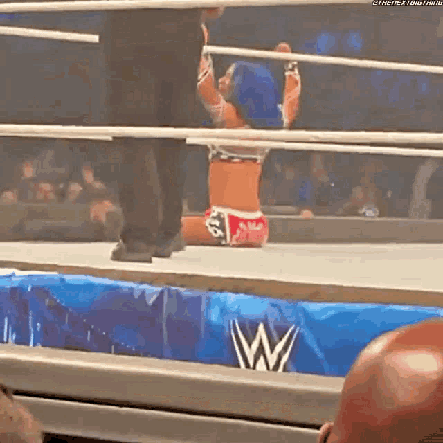 a woman is kneeling down in a wrestling ring while a referee watches .