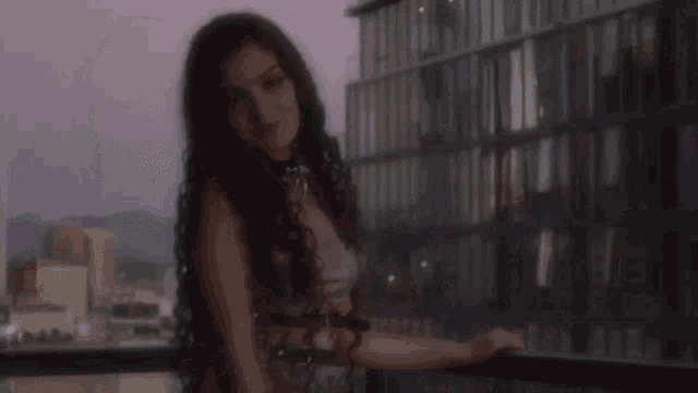 a woman with long hair is standing on a balcony in front of a building